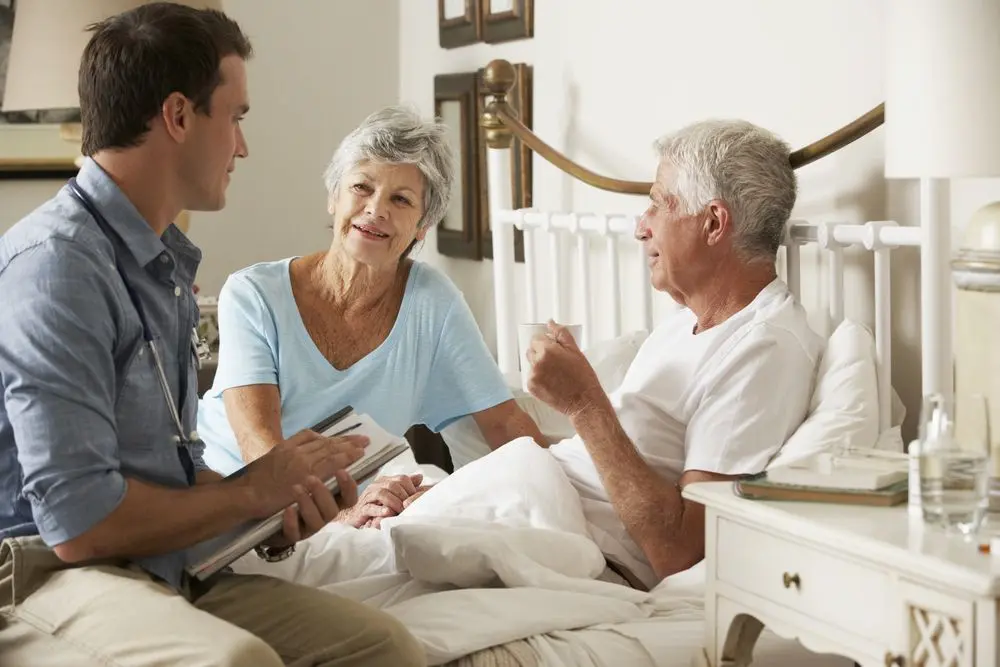 Elderly couple and male carer sat on a bed