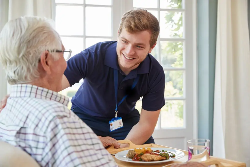Male carer giving a meal to an elderly male resident