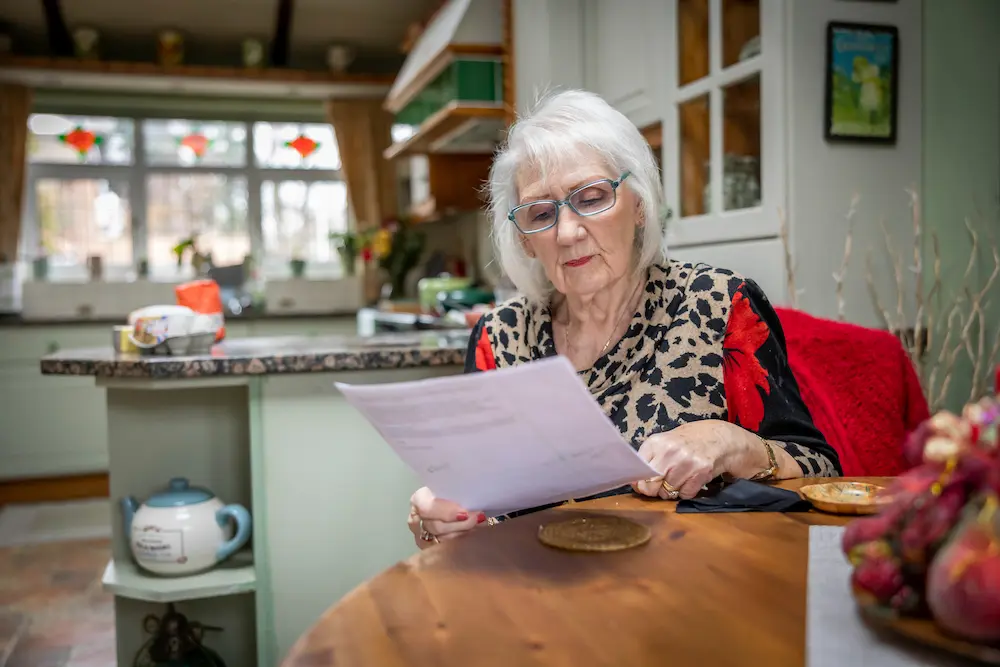 Older woman reading a letter at her kitchen table