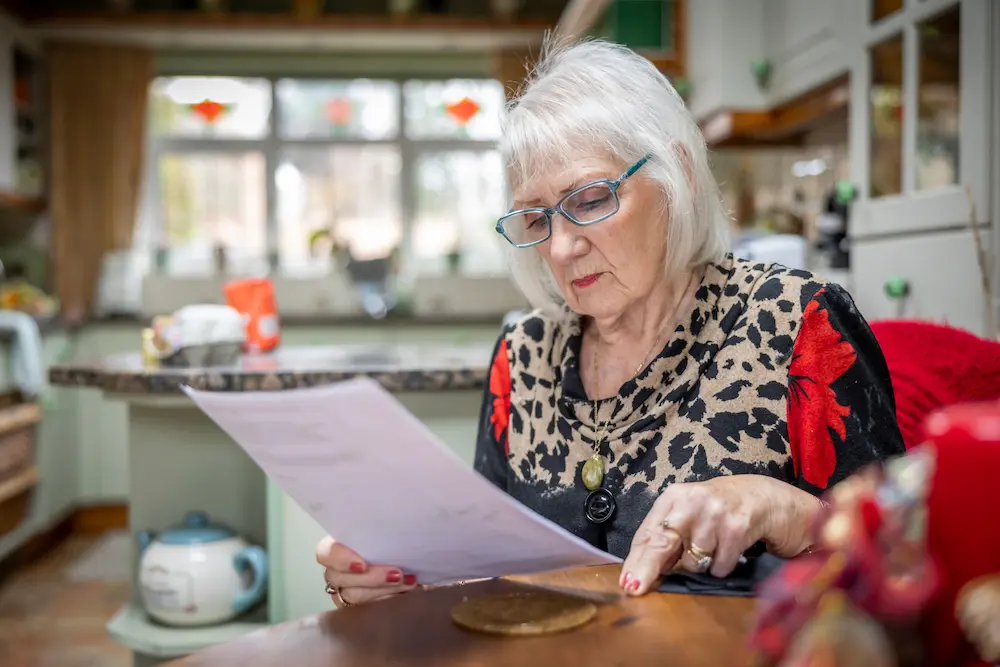 Older woman reading a letter at her kitchen table